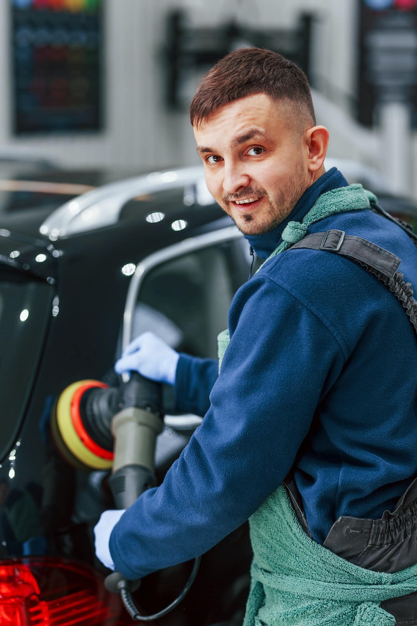 male worker in uniform polishing new modern car conception of service